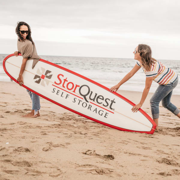 Two women carrying a StorQuest surfboard