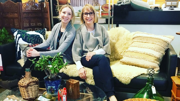 Two smiling women -- Carla and Taylor -- are sitting on a couch in front of a coffee table