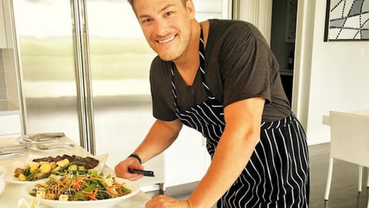 A picture of Paul in a chef apron leaning on a countertop with two vegetable-based meals on white plates.