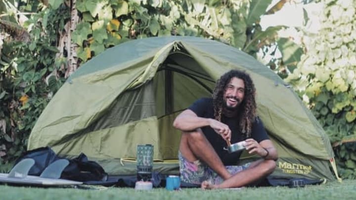 A man named Dr. Cliff K. camping with a tent in the background